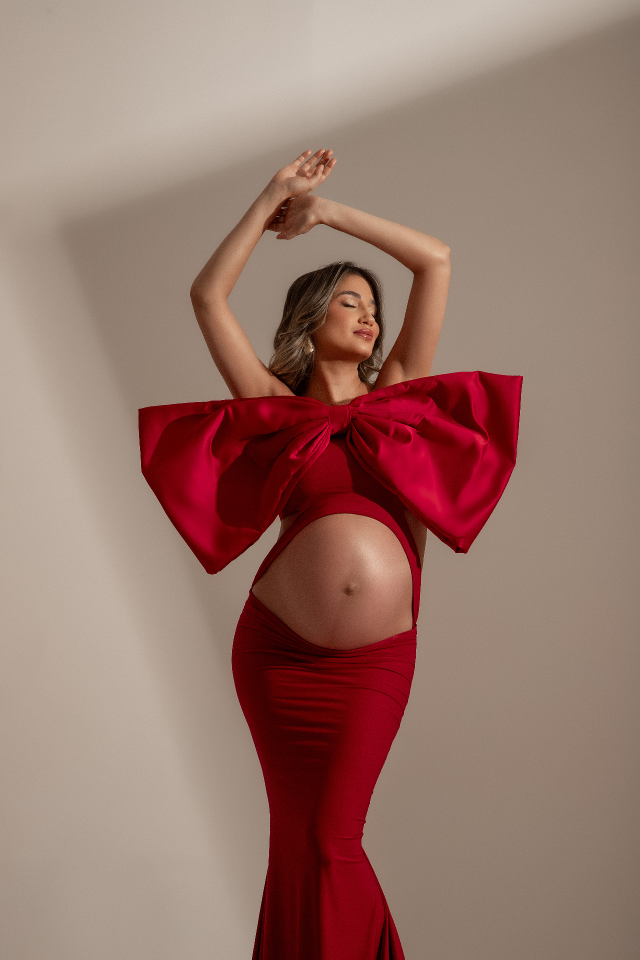 Gestante em vestido vermelho com laço em pose editorial