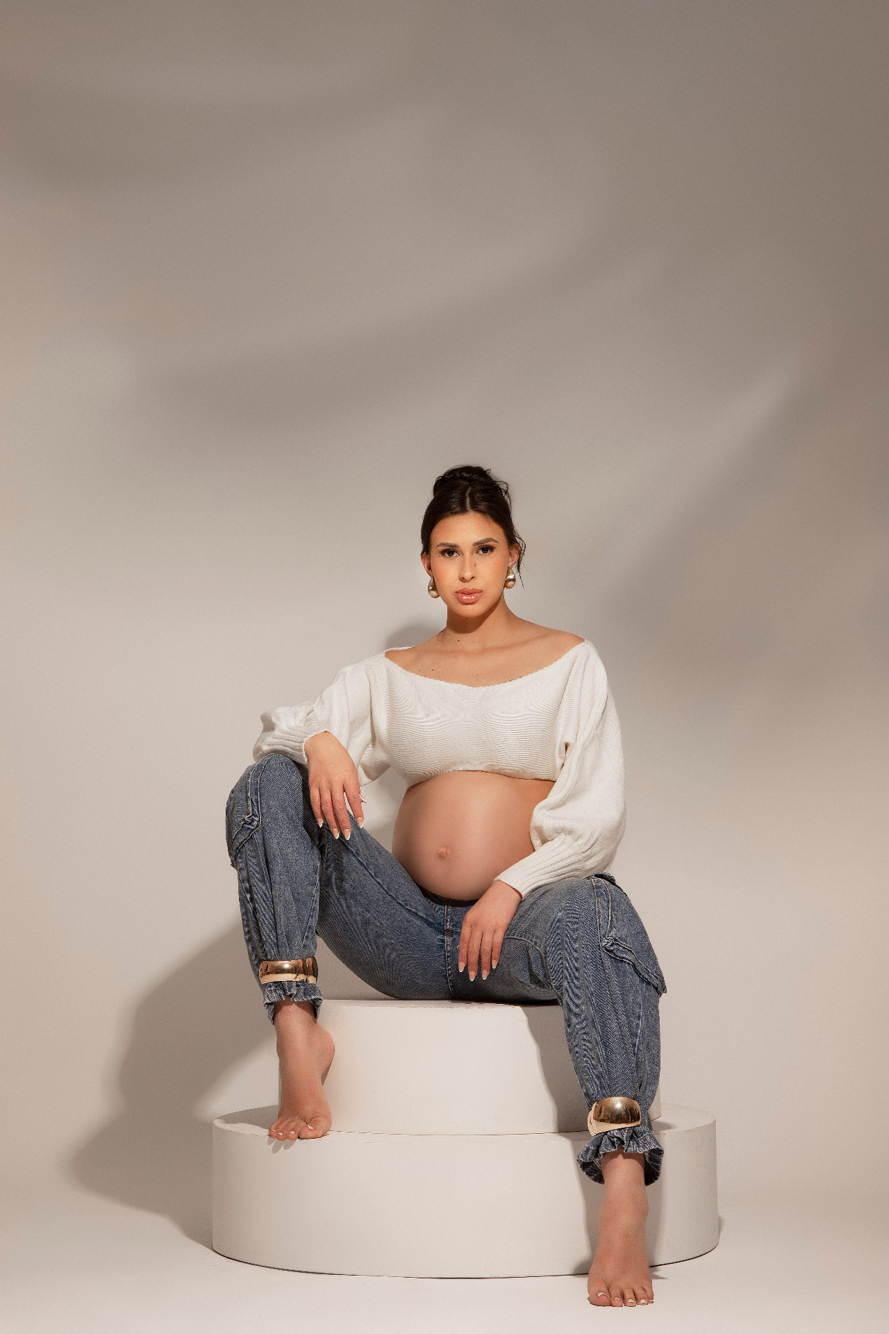 Gestante sentada com blusa branca e jeans em estúdio