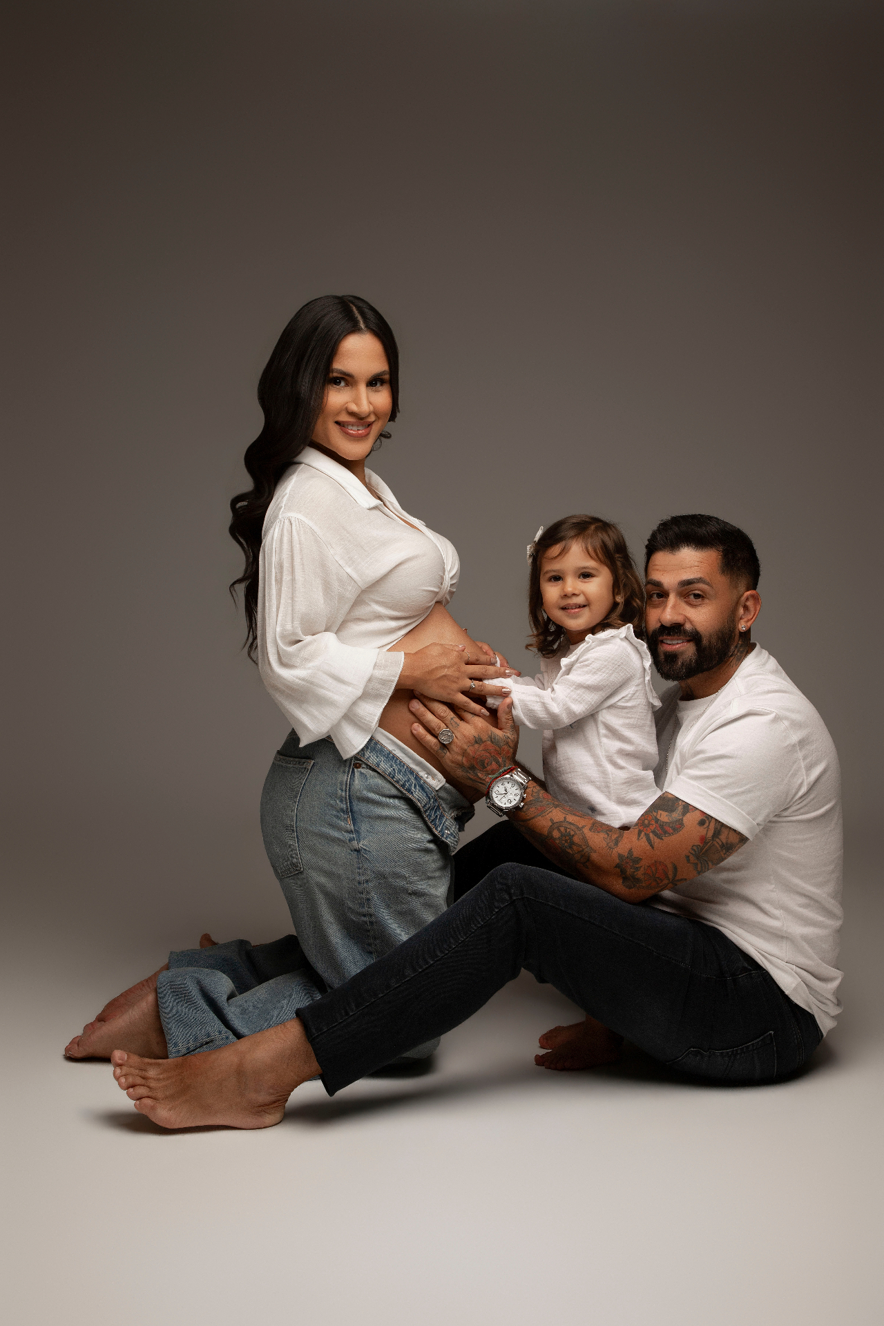 Gestante de branco com marido e filha tocando a barriga