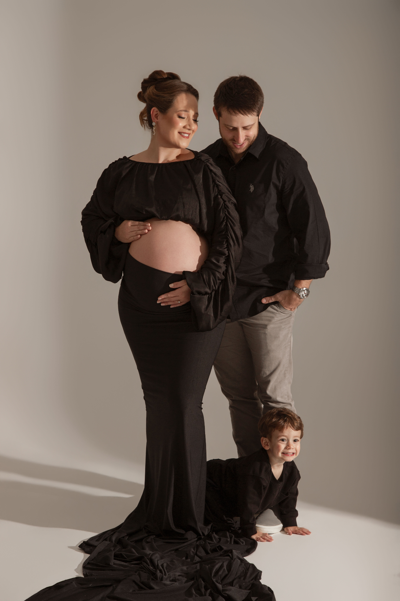 Gestante em vestido preto com marido e filho pequeno