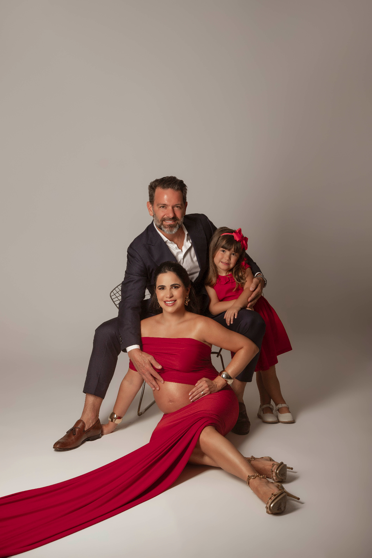 Gestante em vestido vermelho com marido e filha em ensaio elegante