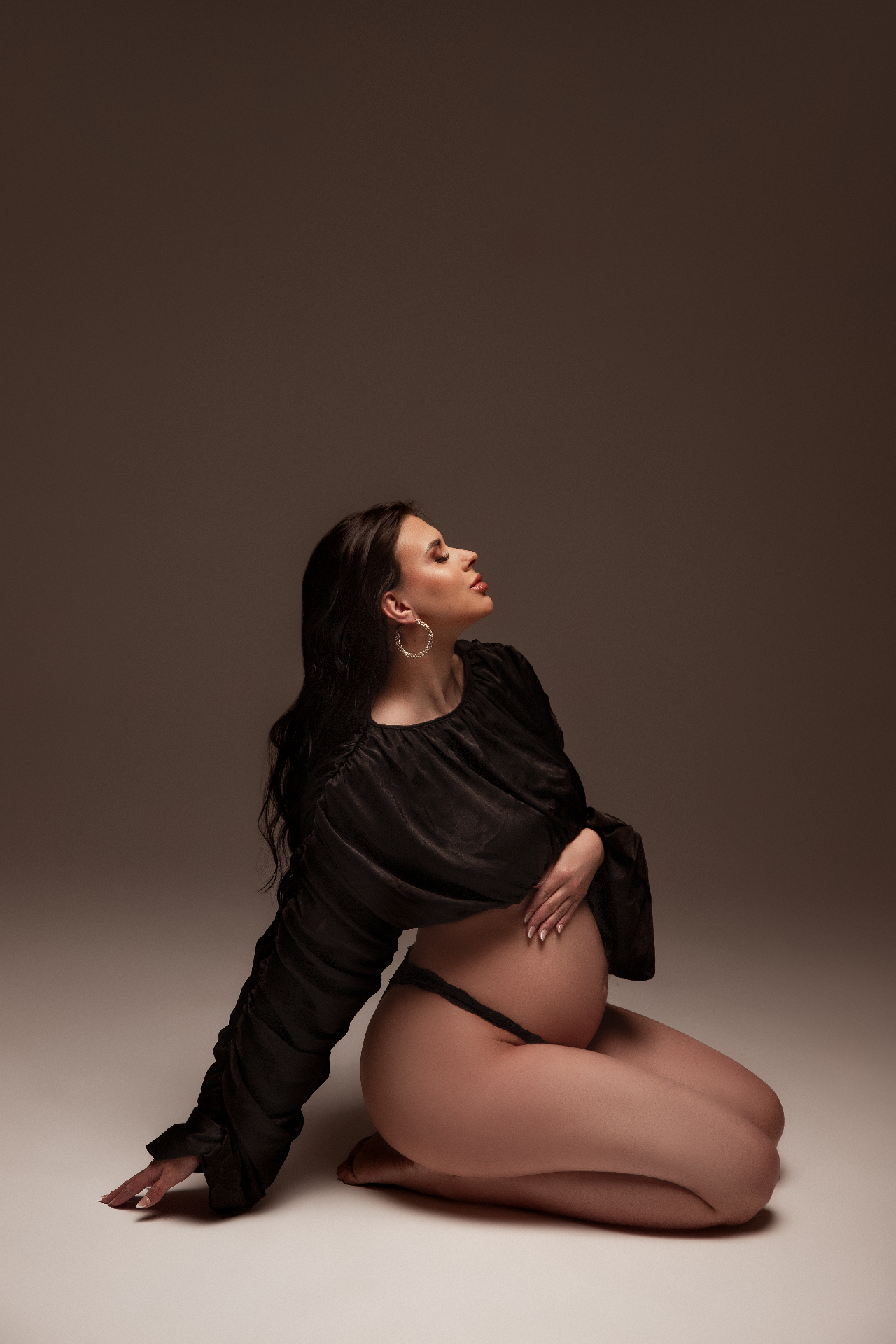 Gestante sentada em pose editorial com camisa preta