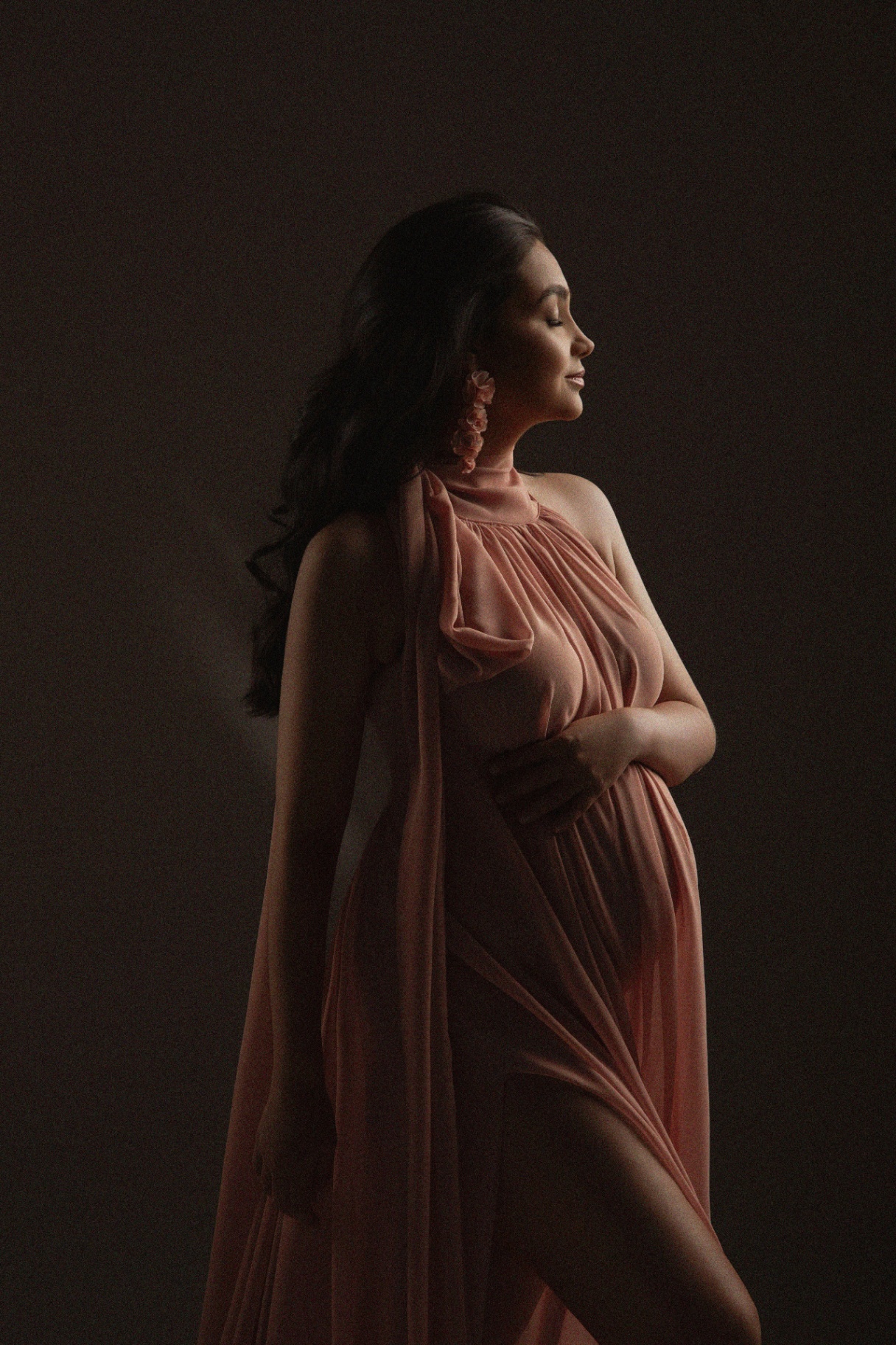 Gestante em vestido rosa fluido com luz dramática